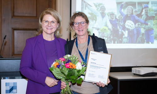 © Fotograf / BBR/BBSR/bundesfoto/BA / Sabine Porschmann, Parlamentarische Staatssekretärin bei der Bundesministerin für Wohnen, Stadtentwicklung und Bauwesen, übereicht Kerstin Mommsen, VAUDE Unternehmenskommunikation, den Bundespreis. Zukunftsfähiges Mobilitätskonzept im ländlichen Raum: VAUDE gewinnt Bundespreis für erfolgreiche nachhaltige Mobilität